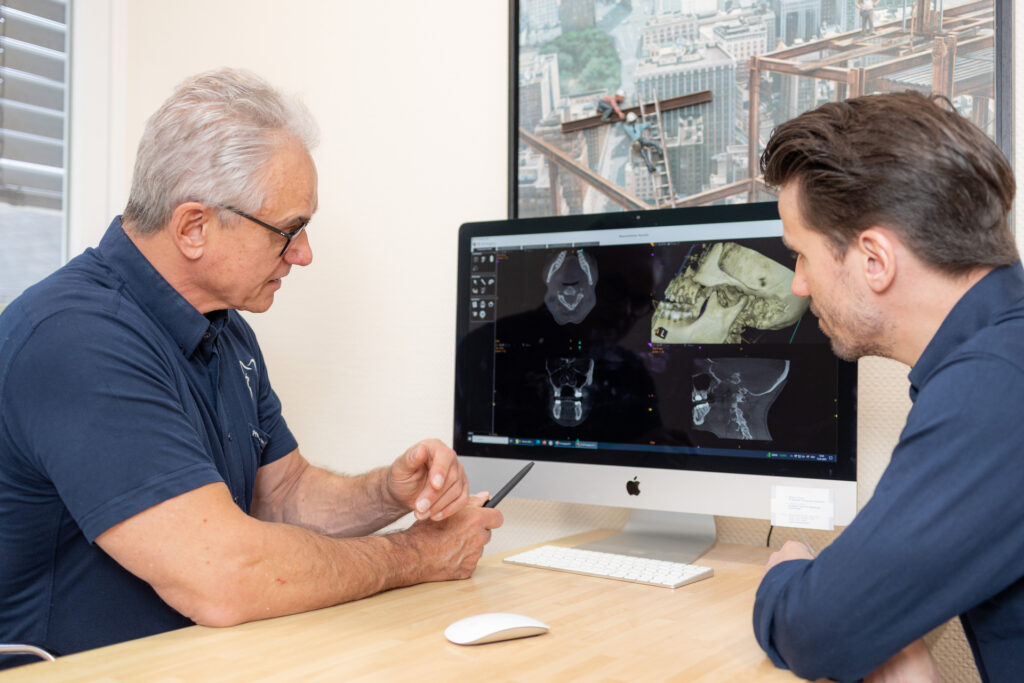 DR. DR. JÜRGEN BRAUNSTEINER und DR. med. dent. Tim BRAUNSTEINER​ schauen sich einen 3D-Scan und Röntgen aufnahmen an
