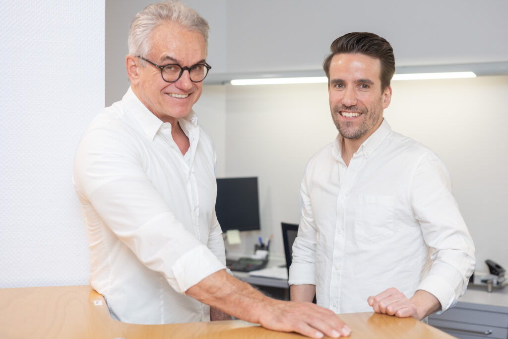 DR. DR. JÜRGEN BRAUNSTEINER und DR. med. dent. Tim BRAUNSTEINER​ an einem Tisch